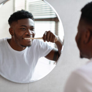 African Guy Cleaning Teeth Smiling To In Mirror In Bathroom