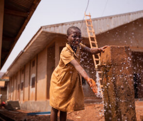 African schoolchild plays splashing water from the tap placed outside in the schoolyard