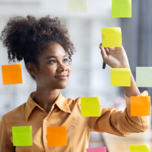 Business female employee with many conflicting priorities arranging sticky notes commenting and